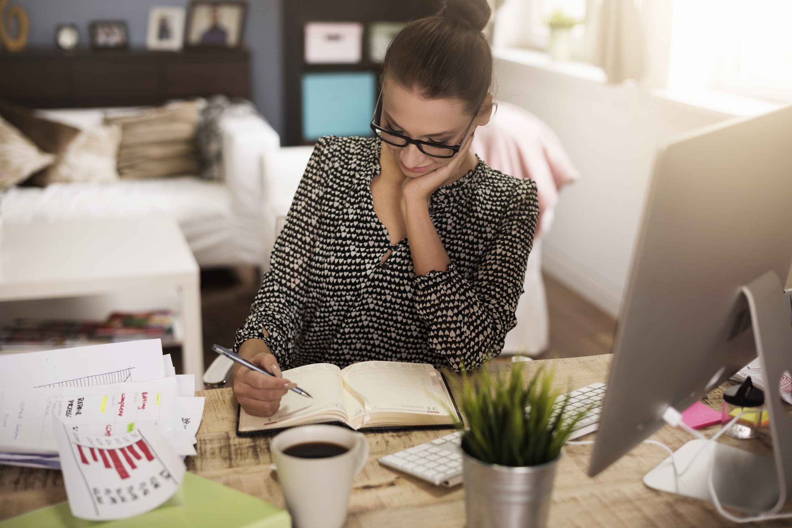 Persona sentada en un escritorio trabajando en una laptop, con una libreta y un bolígrafo en la mano, representando la concentración y la productividad en un entorno de trabajo organizado.