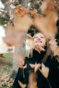 Mujer sonriente disfrutando de un paseo entre las hojas que caen en un entorno natural.
