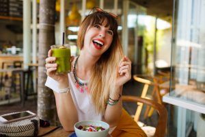Mujer sonriente y radiante disfrutando de un jugo verde detox, experimentando los beneficios de una dieta para desintoxicar el cuerpo.