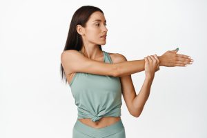 Mujer realizando un estiramiento de hombro para mejorar la movilidad y aliviar la tensión muscular.