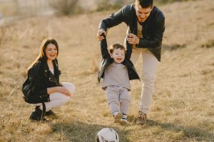 Padres con su hijo jugando afuera con una pelota de futbol.
