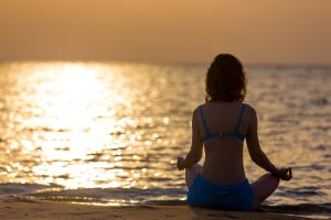 Mujer meditando en la playa, simbolizando la gestión de las emociones a través de la relajación y el equilibrio personal.