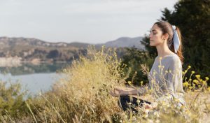 Mujer meditando en la naturaleza, una manera efectiva para reducir el estrés.