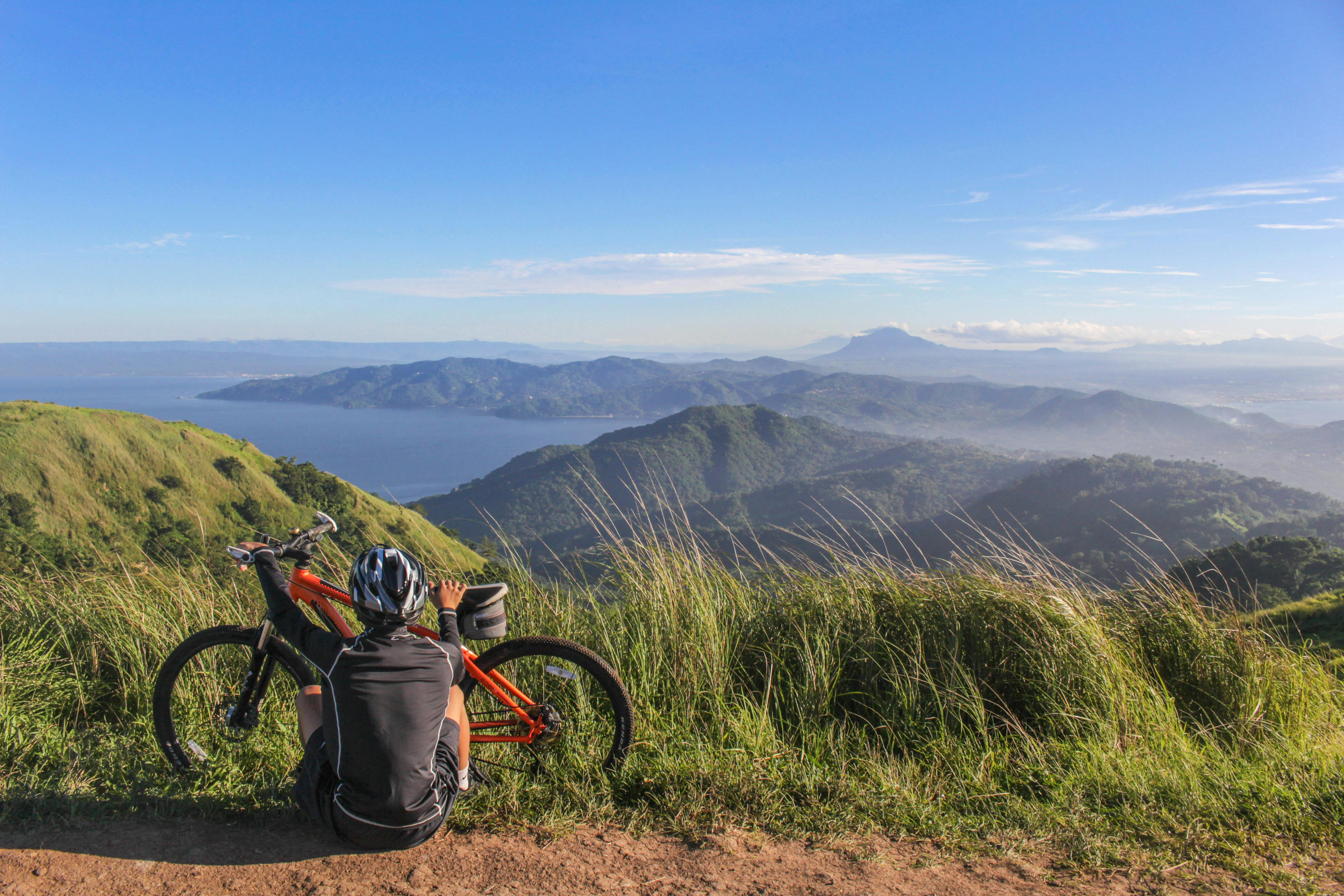 Persona montando en bicicleta en entorno natural montañoso con vista al mar, promoviendo hábitos sostenibles.