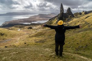 Persona abriendo los brazos desde una montaña, con un paisaje montañoso y de mar de fondo. Explorando la expansión espiritual desde la cima de la montaña, conectando con la naturaleza - Las 4 leyes de la espiritualidad.