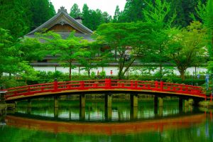 Imagen de un hermoso jardín japonés con un tranquilo lago, un puente arqueado y una casa tradicional japonesa al fondo. Esta imagen representa la serenidad y la belleza de la cultura japonesa en conexión con la naturaleza.