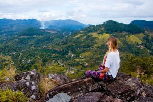 mujer meditando tranquila con vista a la naturaleza, rodeado de montañas.