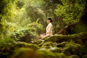 Mujer meditando en la naturaleza, practicando el autocuidado.