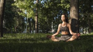 Una joven practica mindfulness en posición de loto sobre el césped.