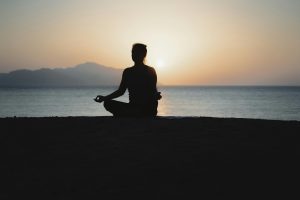 Mujer meditando frente al mar al atardecer: reflejo de serenidad en las Meditaciones Marco Aurelio