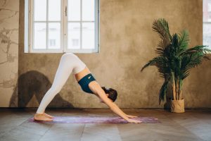 Mujer realizando la postura del Perro Boca Abajo (Adho Mukha Svanasana) para estirar y fortalecer los músculos de todo el cuerpo. Esta pose de yoga alivia el estrés y promueve el bienestar físico al estirar las caderas, las piernas y la espalda.
