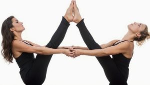 Dos mujeres realizando la postura del barco en pareja.