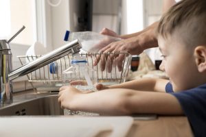 Niño llenando una botella reutilizable con agua del grifo, resaltando la importancia de la purificación del agua en casa para una vida saludable.