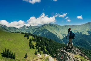 Persona disfrutando del senderismo en la cima de una montaña, expresando su amor por la naturaleza al contemplar el paisaje.