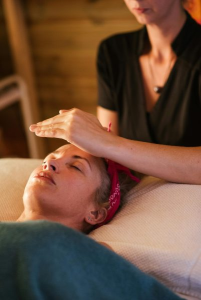 Mujer realizando una sesión de Reiki en el rostro de una paciente que disfruta de la sesión con los ojos cerrados.