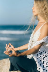 Mujer meditando en la playa: practica la atención plena para cultivar la paz interior y reducir el estrés.