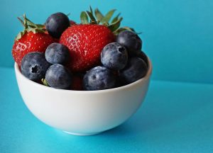Arándanos y fresas en un cuenco sobre fondo celeste. Alimentos antiinflamatorios ricos en antioxidantes.