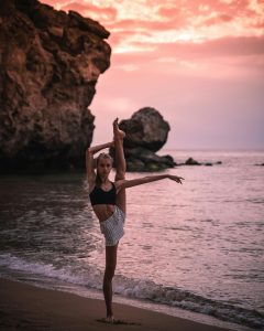 Adolescente realizando una postura de yoga en la playa, con el mar de fondo. La imagen muestra flexibilidad y serenidad en la práctica.