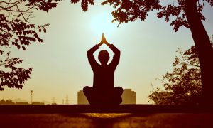 Persona meditando con las manos juntas sobre la cabeza, conectando con el sol y la espiritualidad.