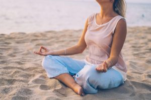 mujer practicando meditaciones en la playa, con mucha paz.