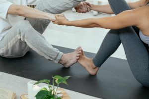 una pareja tomada de las manos y se chocan los pies sobre una esterilla de yoga, practicando una postura de yoga.