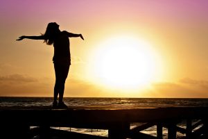 Una joven con los brazos abiertos hacia el cielo, recibiendo la luz del sol en su cuerpo.