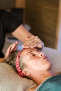 Mujer practicando Terapia Alternativa Reiki en el rostro de una paciente que disfruta de la sesión con los ojos cerrados.